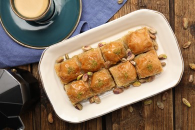 Delicious baklava with pistachios, hot drink and scattered nuts on wooden table, flat lay