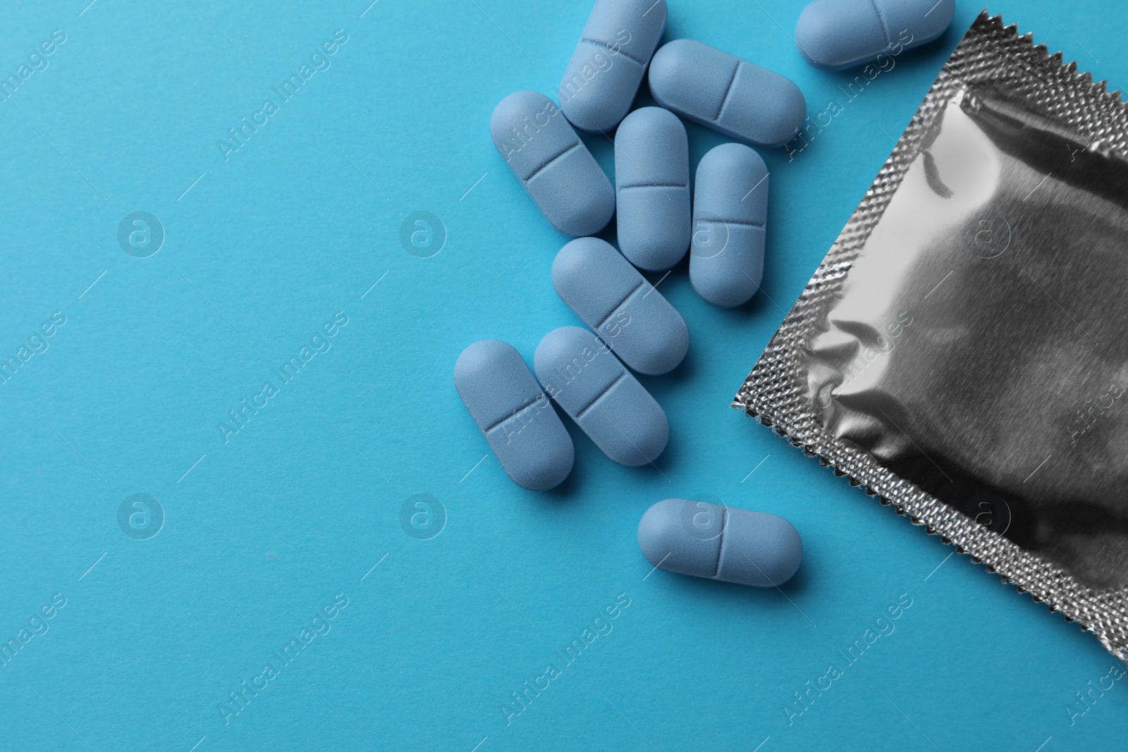 Photo of Pills and condom on light blue background, flat lay with space for text. Potency problem concept