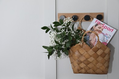 Photo of Stylish wicker basket with bouquet of flowers and magazine hanging on wooden rack indoors, space for text
