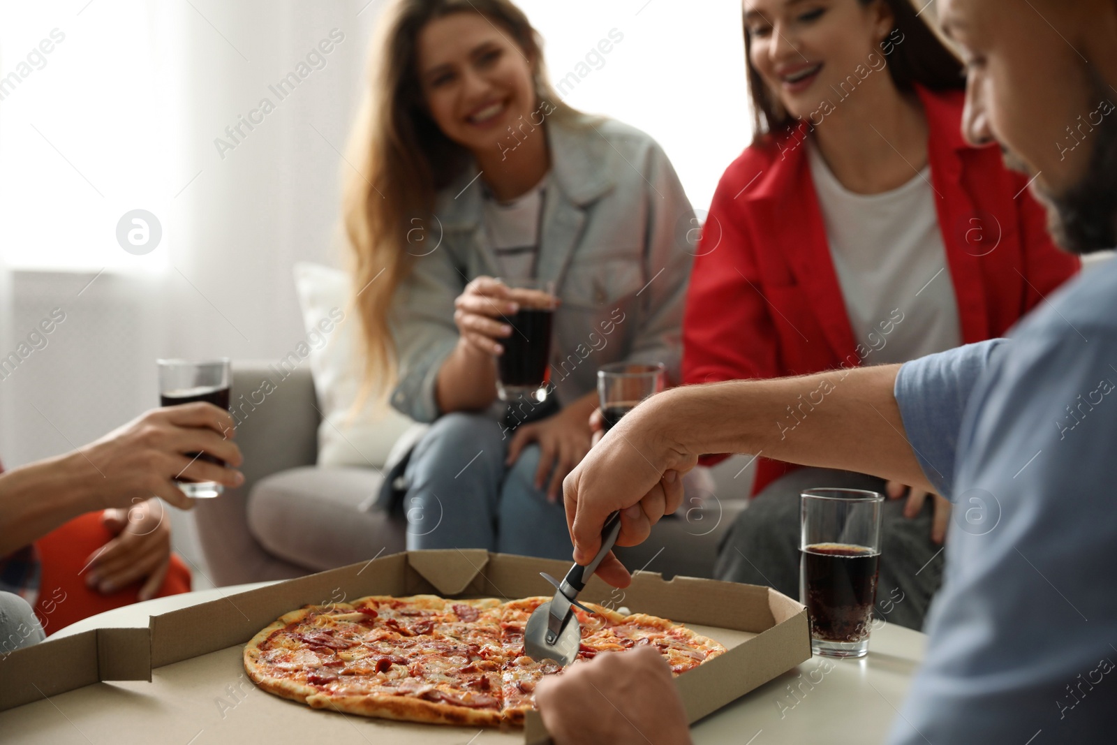 Photo of Man cutting fresh pizza on table and friends indoors, closeup