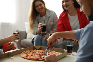Man cutting fresh pizza on table and friends indoors, closeup