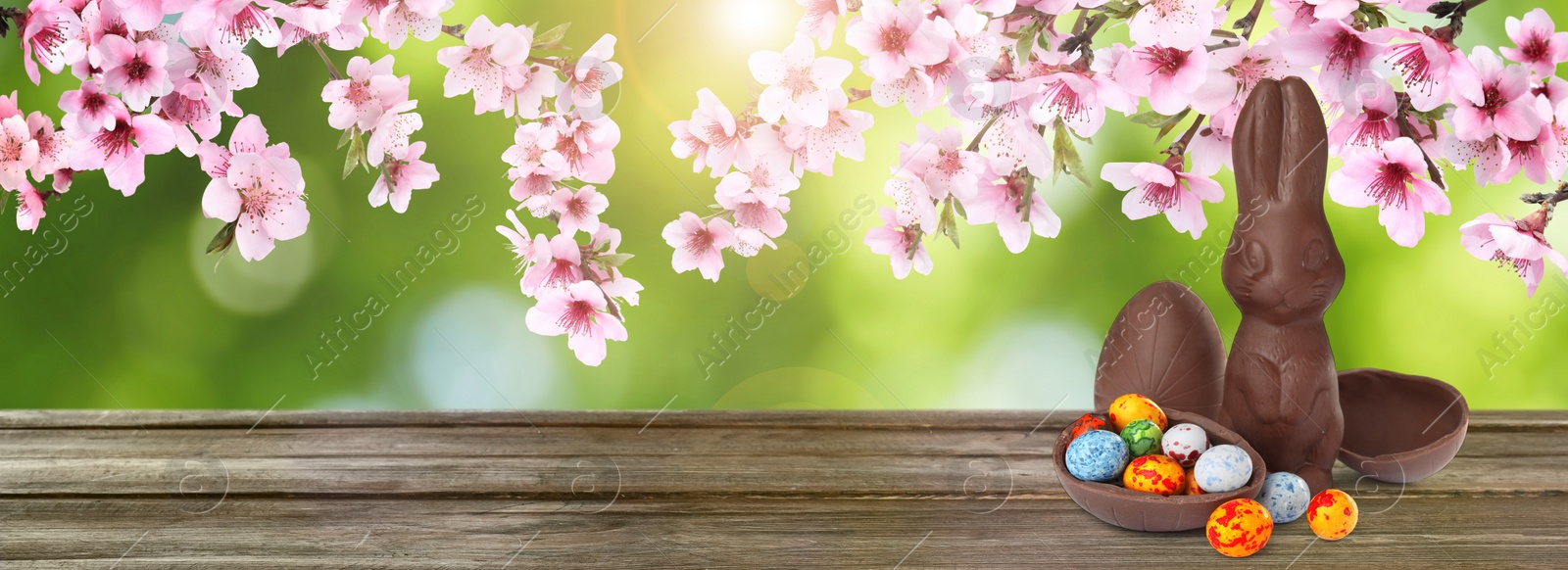 Image of Sweet chocolate bunny and colorful eggs on wooden table outdoors, banner design. Easter celebration