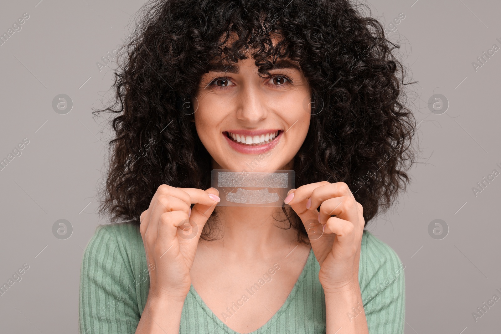 Photo of Young woman holding teeth whitening strips on grey background