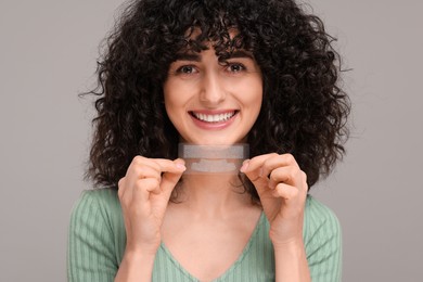 Photo of Young woman holding teeth whitening strips on grey background
