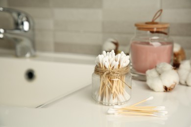 Photo of Cotton swabs and flowers on sink in bathroom, space for text