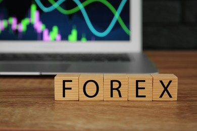 Photo of Word Forex made with cubes and laptop on wooden table