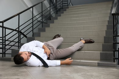 Photo of Man fallen down stairs suffering from pain indoors, space for text