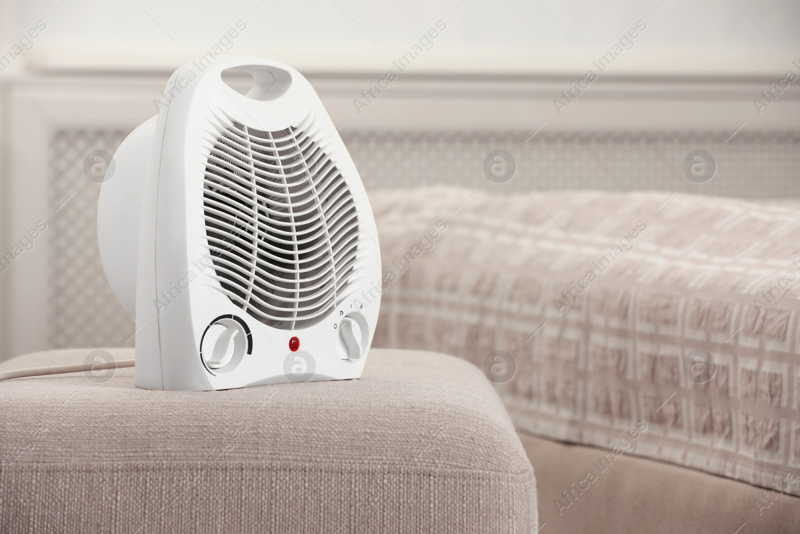 Photo of Modern electric fan heater on pouf in cozy room. Space for text