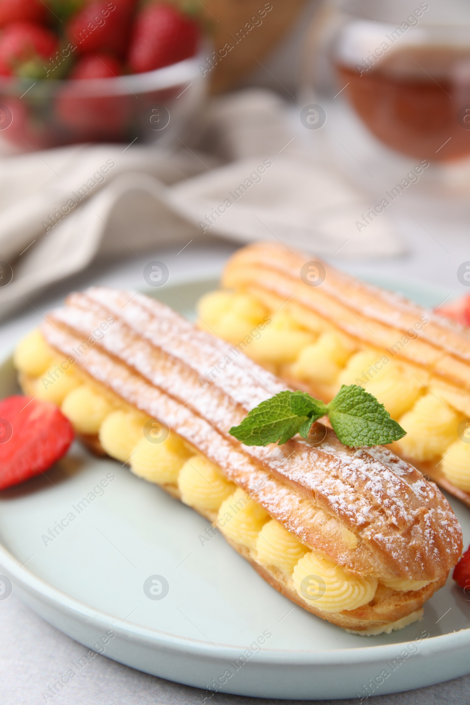 Photo of Delicious eclairs filled with cream, strawberry and mint on table, closeup