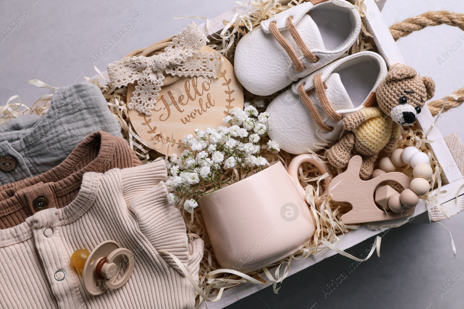 Photo of Wooden box with baby clothes, booties and toys on grey background, top view