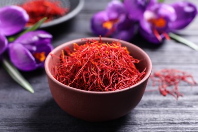 Photo of Dried saffron in bowl and crocus flowers on black wooden table, closeup