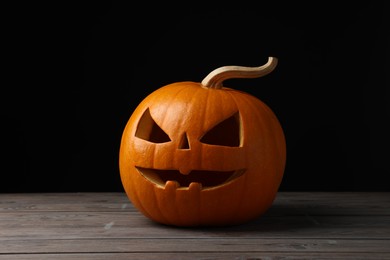 Photo of Scary jack o'lantern made of pumpkin on wooden table against black background. Halloween traditional decor