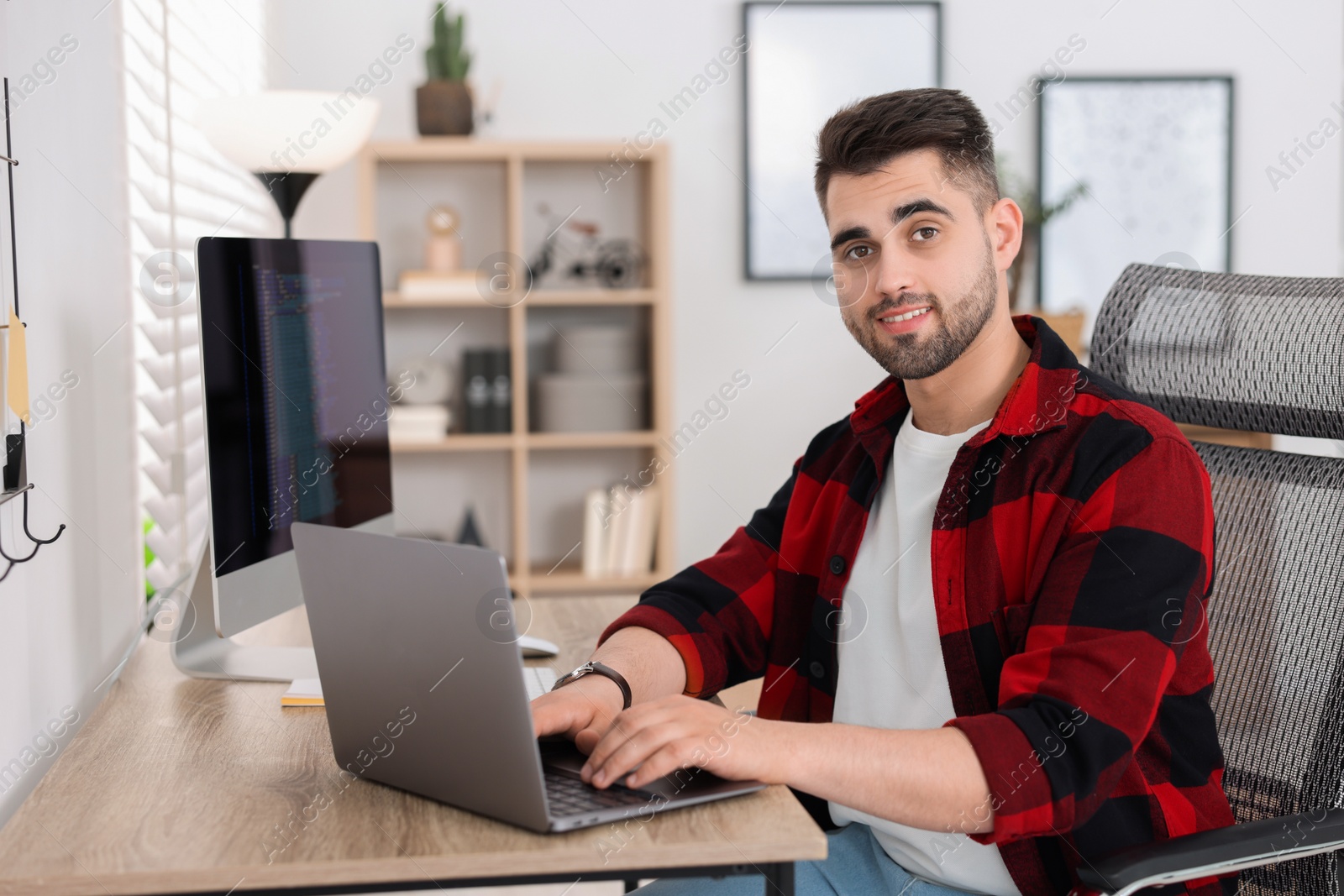 Photo of Happy young programmer working with laptop in office