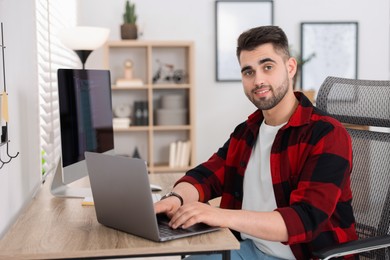 Photo of Happy young programmer working with laptop in office