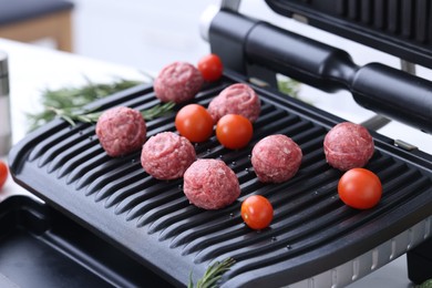 Photo of Meatballs, tomatoes and rosemary on electric grill, closeup