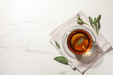 Photo of Cup of aromatic herbal tea with sage on white marble table, top view. Space for text
