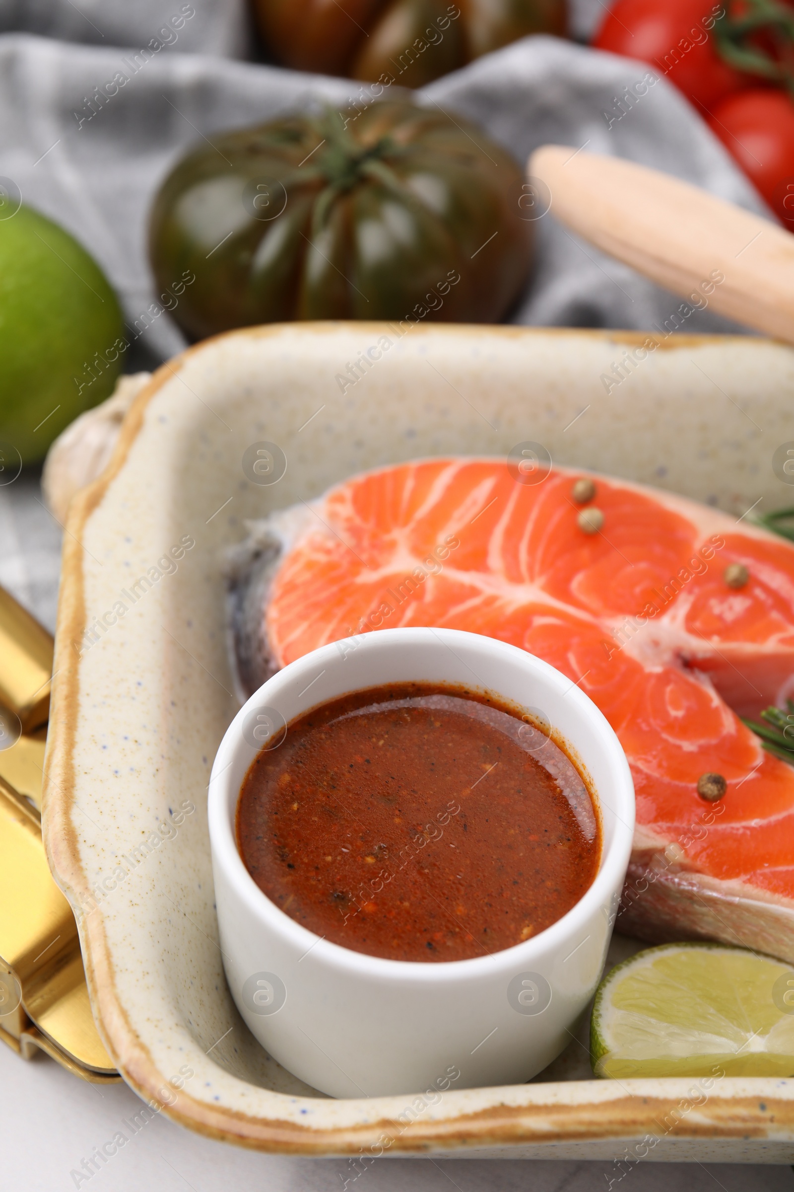 Photo of Fresh marinade, fish and lime in baking dish on table, closeup