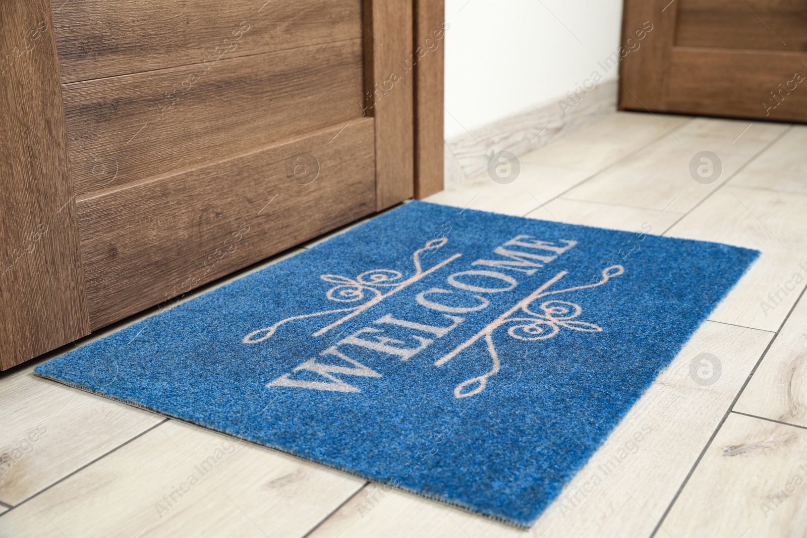 Photo of Beautiful blue doormat with word Welcome on floor near entrance