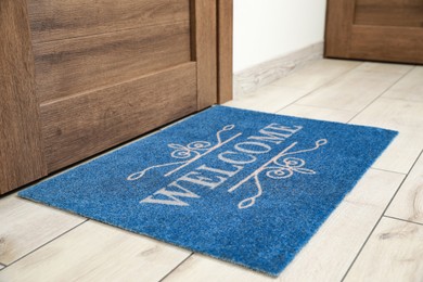 Photo of Beautiful blue doormat with word Welcome on floor near entrance