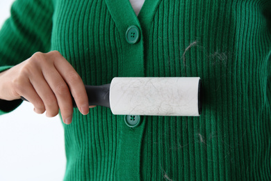 Woman removing hair from green knitted jacket with lint roller on light background, closeup