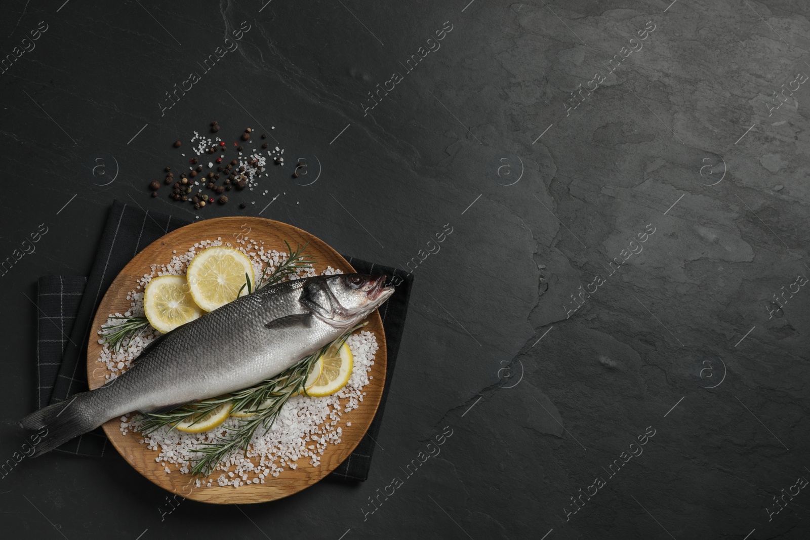 Photo of Sea bass fish and ingredients on black table, flat lay. Space for text