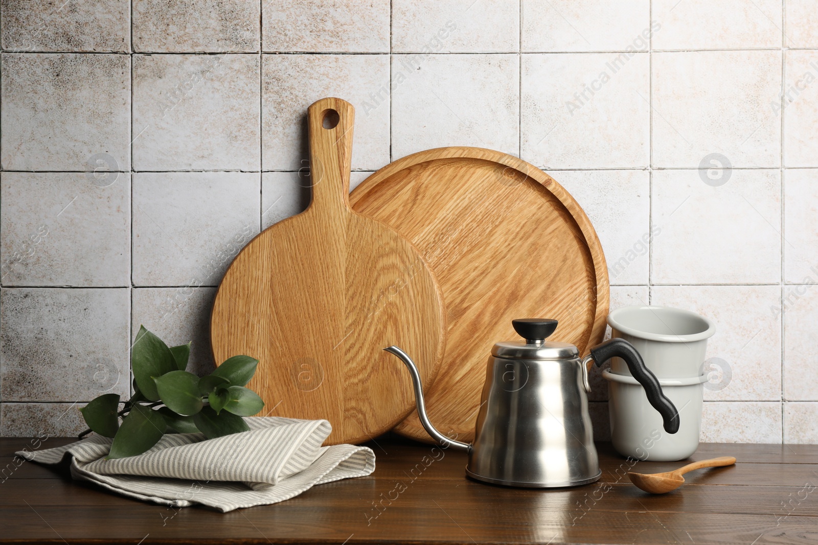 Photo of Wooden cutting boards, dishware and towel on table near tiled wall