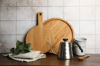 Photo of Wooden cutting boards, dishware and towel on table near tiled wall