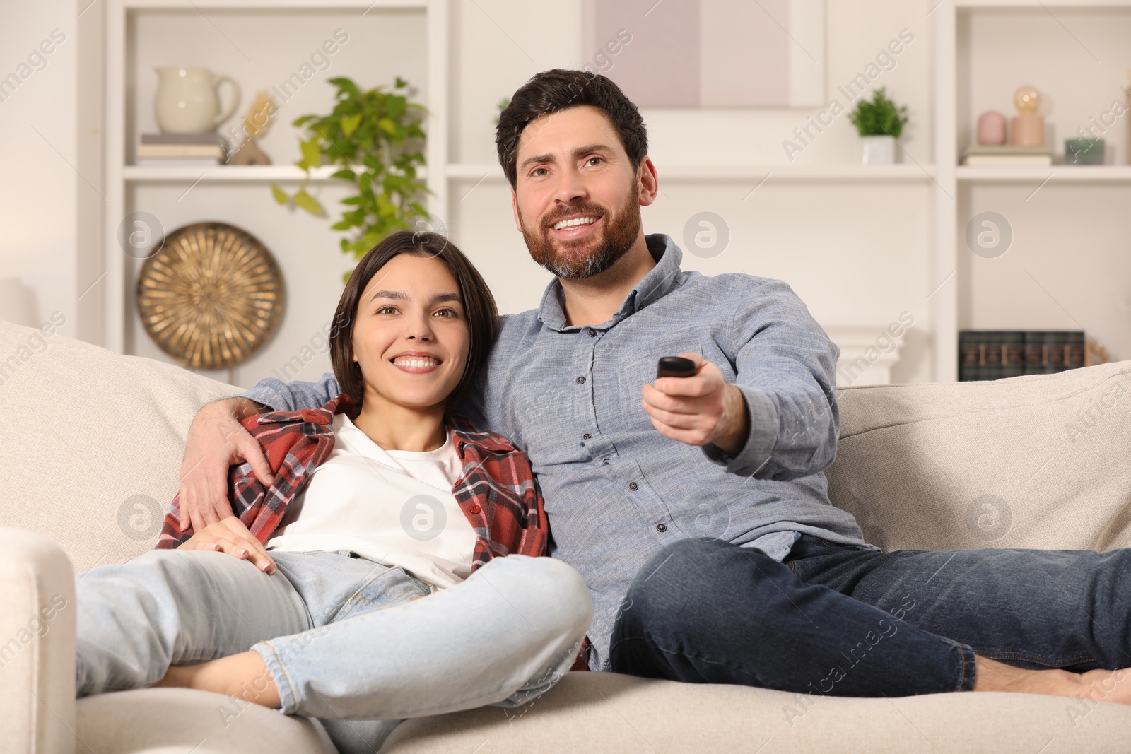 Photo of Happy couple watching TV on sofa at home