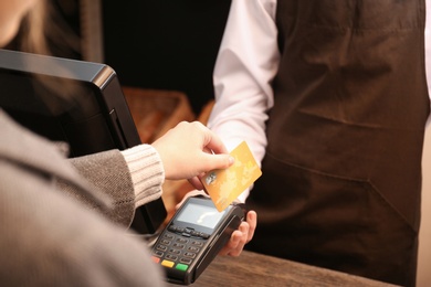 Photo of Woman with credit card using payment terminal at shop, closeup