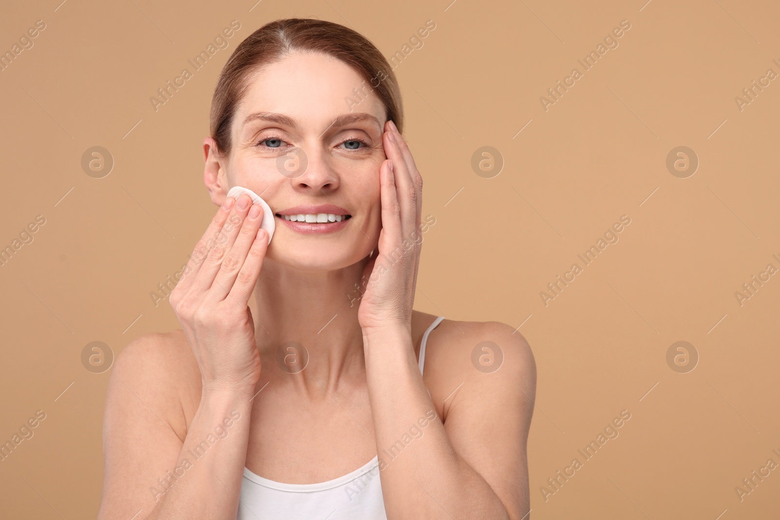 Photo of Beautiful woman removing makeup with cotton pad on beige background, space for text