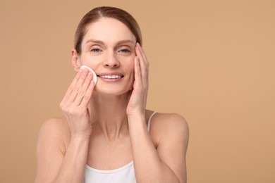 Beautiful woman removing makeup with cotton pad on beige background, space for text