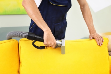 Photo of Dry cleaning worker removing dirt from sofa indoors