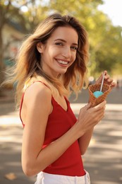 Photo of Happy young woman with delicious ice cream in waffle cone outdoors