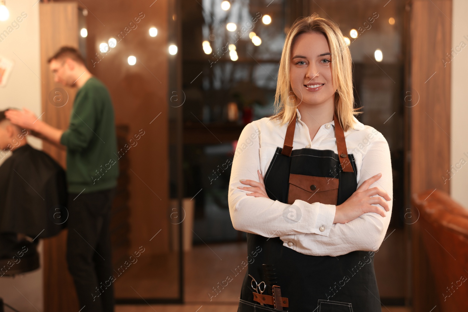 Photo of Portrait of professional hairdresser wearing apron in beauty salon, space for text