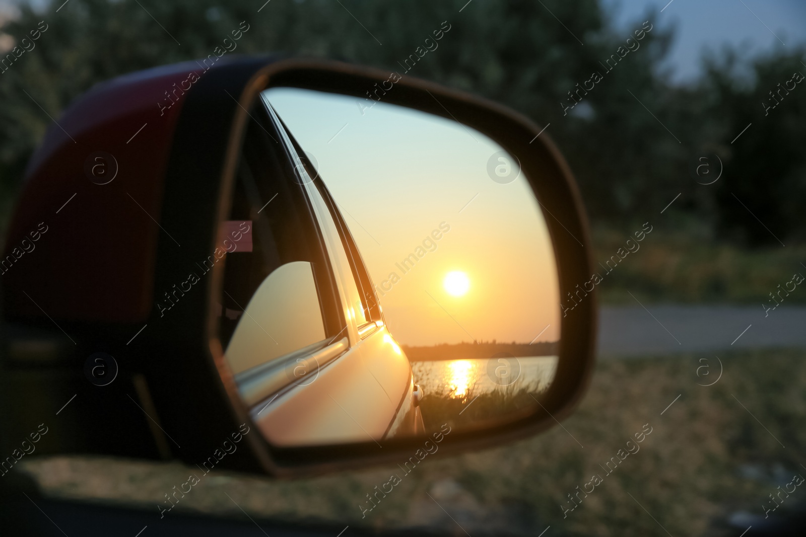 Photo of Reflection of landscape with beautiful sunset over calm river in car side view mirror, closeup