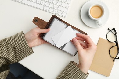 Woman holding leather business card holder with blank cards at white table, top view