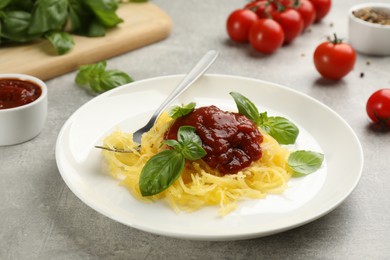 Photo of Tasty spaghetti squash with tomato sauce and basil 
served on light grey table