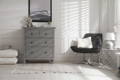 Photo of Stylish room interior with grey chest of drawers and comfortable chair