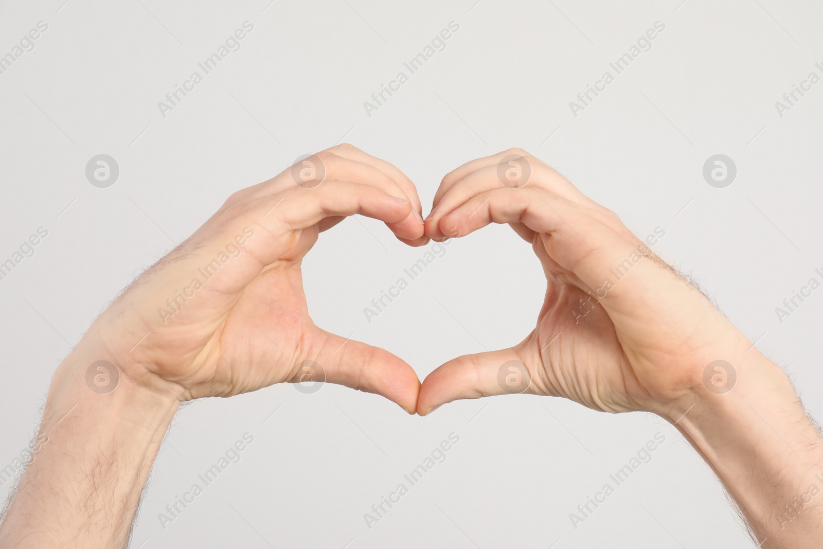 Photo of Man making heart with his hands on light background, closeup