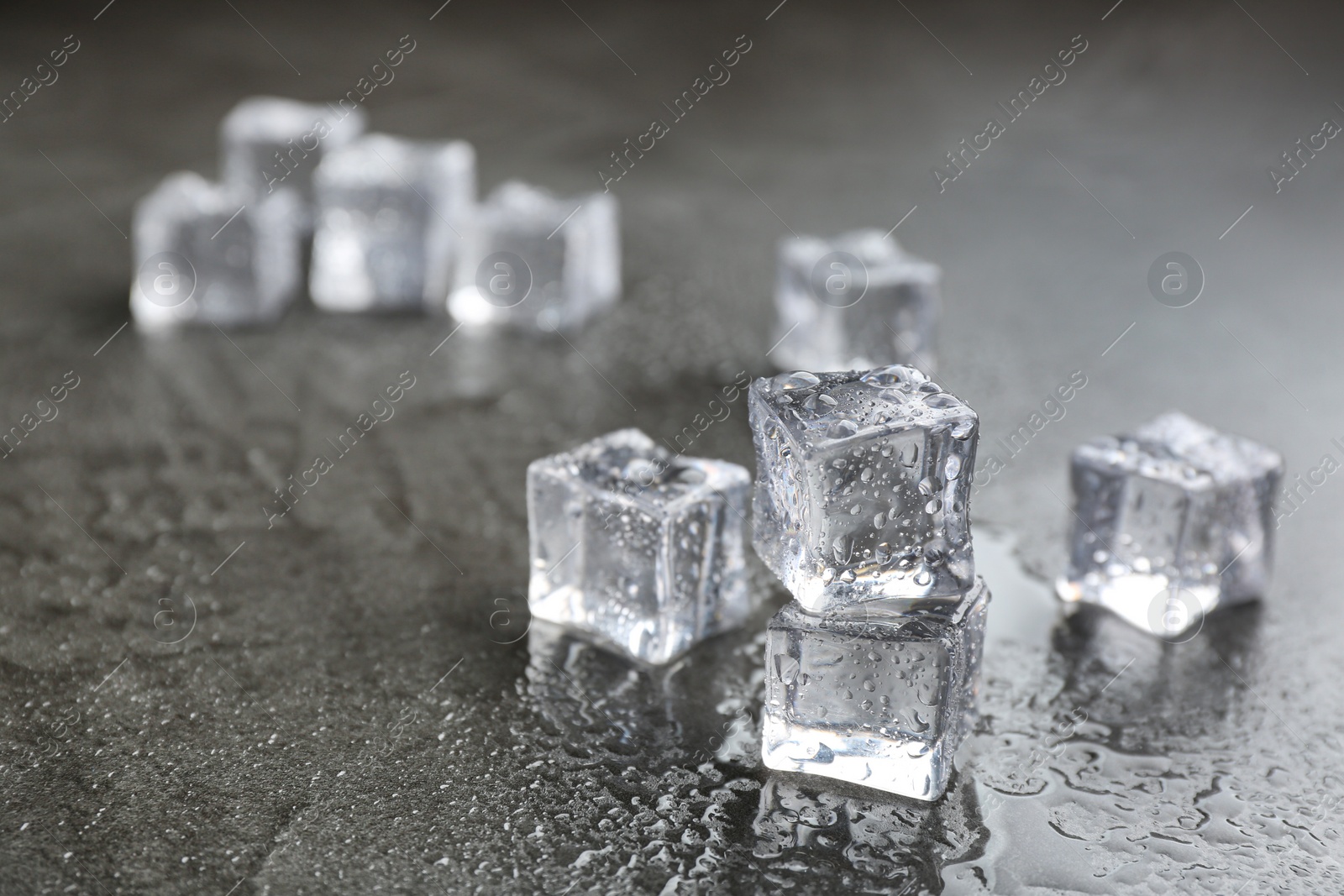 Photo of Crystal clear ice cubes on grey stone table. Space for text