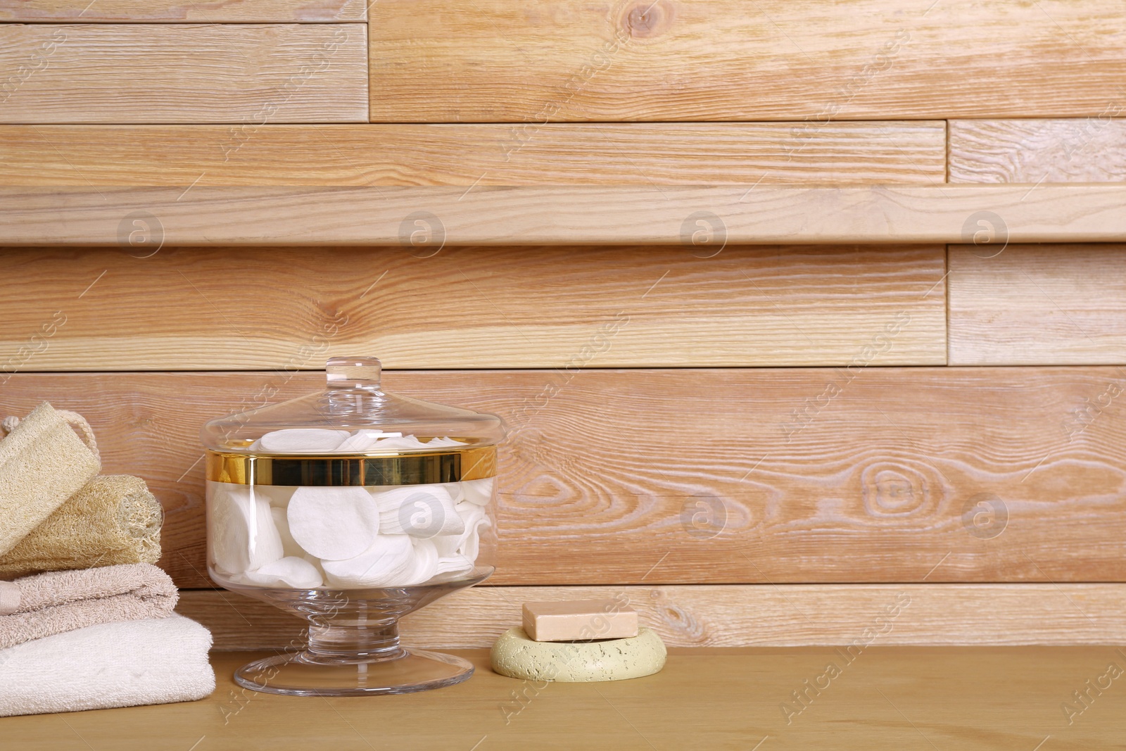 Photo of Composition of glass jar with cotton pads on table near wooden wall. Space for text