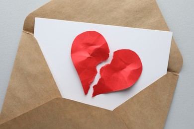 Envelope with halves of torn red paper heart on white background, top view. Broken heart