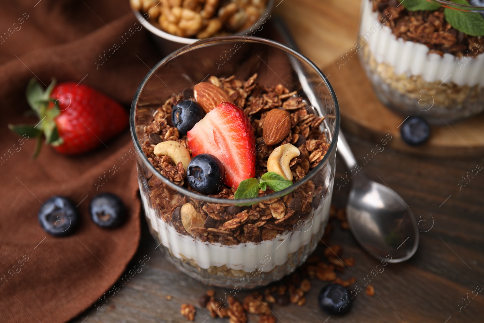 Photo of Tasty granola with berries, nuts and yogurt in glass on wooden table, closeup