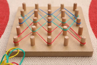 Photo of Wooden geoboard with rubber bands on carpet, closeup. Educational toy for motor skills development