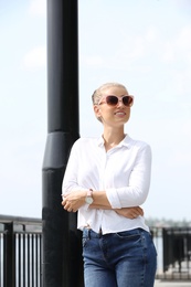 Photo of Beautiful young woman with sunglasses standing at pier. Joy in moment