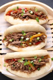 Photo of Delicious gua bao in bamboo steamer on black table, top view