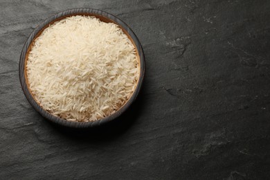 Photo of Raw basmati rice in bowl on black table, top view. Space for text