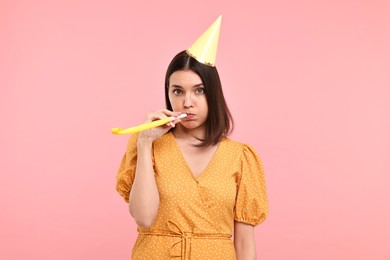 Photo of Young woman in party hat with blower on pink background