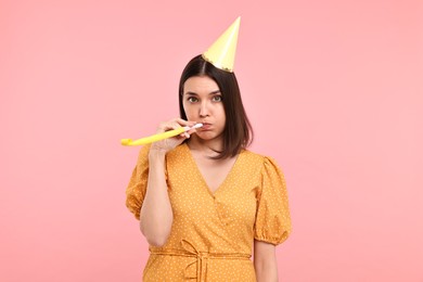 Young woman in party hat with blower on pink background