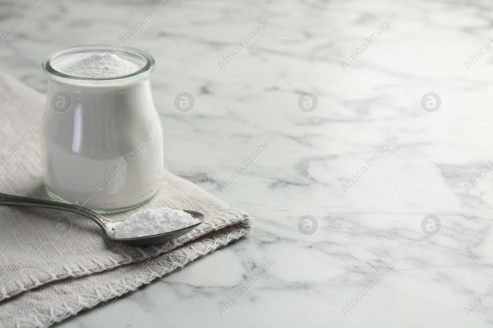 Photo of Baking powder in jar and spoon on white marble table, space for text